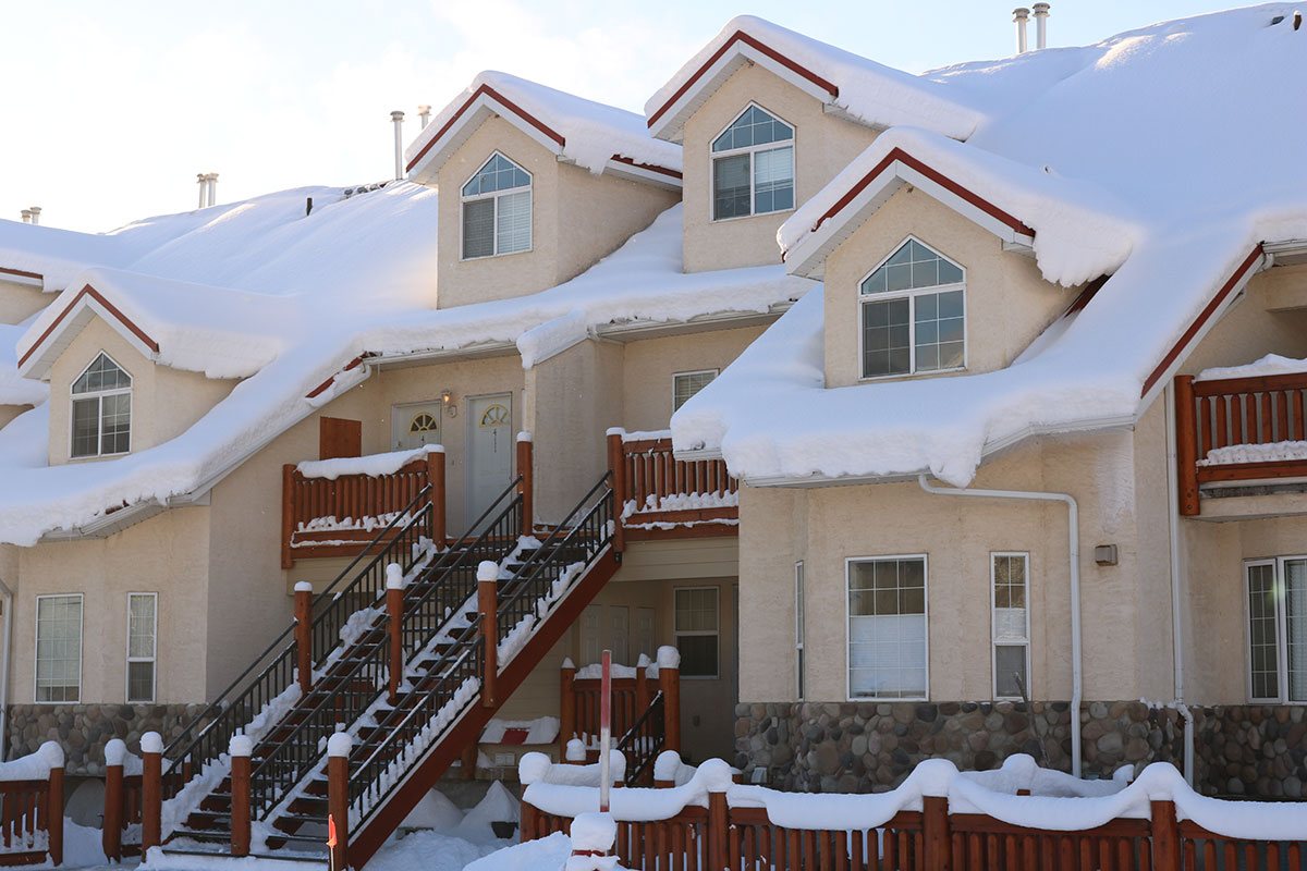 The exterior of a snow-covered multi-level condominium unit at Stanford Fernie Resort with a steel rod staircase leading to entrances protected by auburn brown wood balconies.