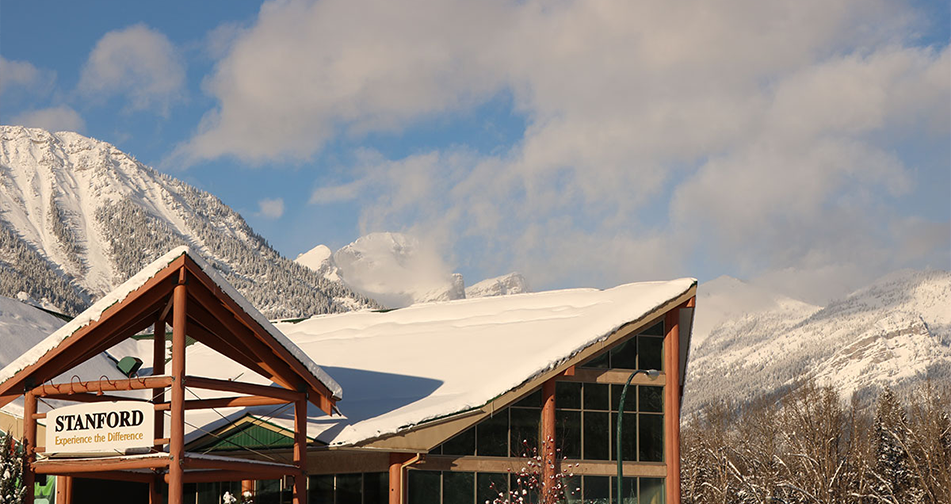 A view of the snow covered gabled rooftop and gabled portico structures of the Stanford Fernie Resort set against the towering  snow laden summit of the Rocky Mountains in BC.