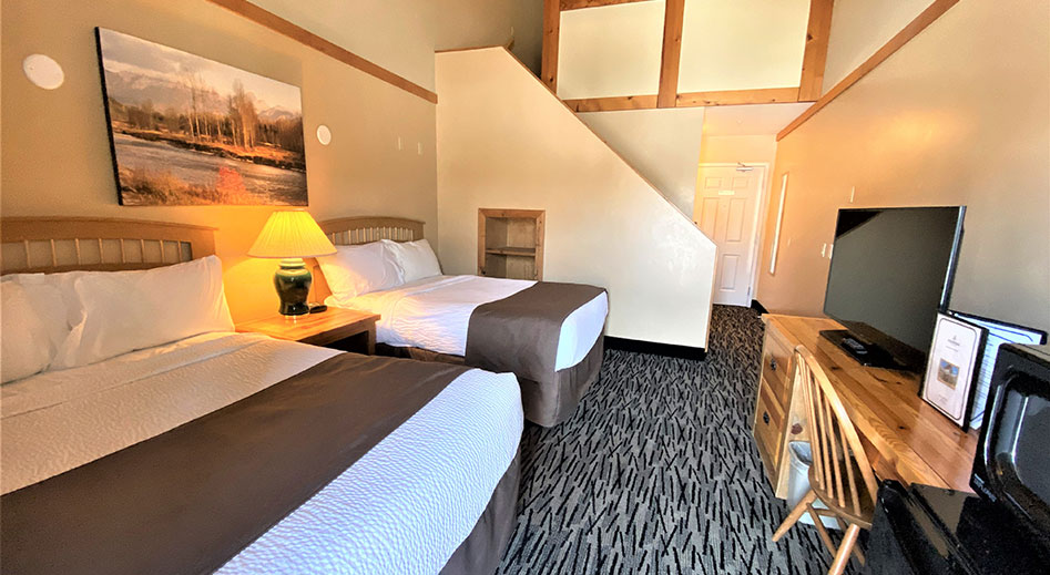 The family suite at Stanford Fernie Resort features a king sized bed with flowered print cover, two bedside tables and lamps and an oil painting of the Elk River hung above.