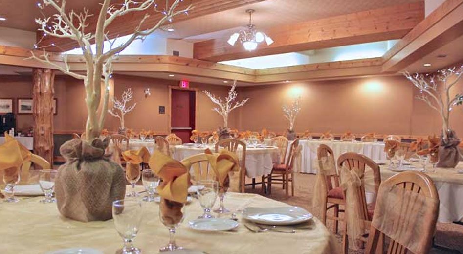 The Banquet Room at the Stanford Fernie Resort features elegantly set banquet tables with barren trees as centerpieces with its' branches decorated with lights and a brown burlap wrapping used as a base stand.