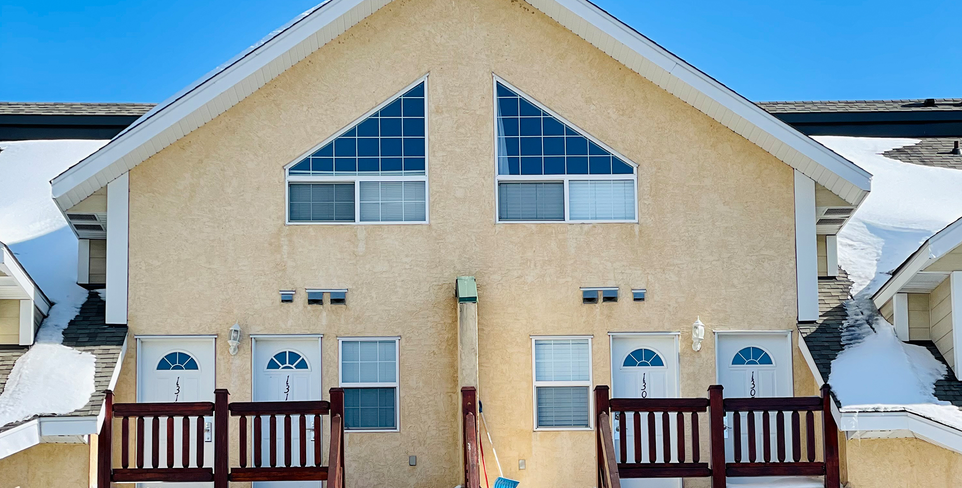 The exterior view of unit #400, a condominium unit at the Stanford Fernie Resort features off white color walls and cobblestone accent trim, bay windows and red-brown wood posts on the staircase and balcony.