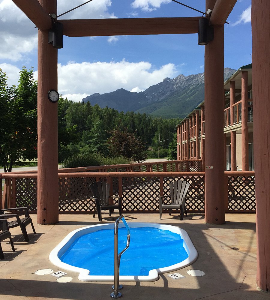 The whirlpool area at Stanford Fernie Resort featuring a round shaped whirlpool surrounded by brown scalloped back patio chairs with an overhead cover made of large wood posts.