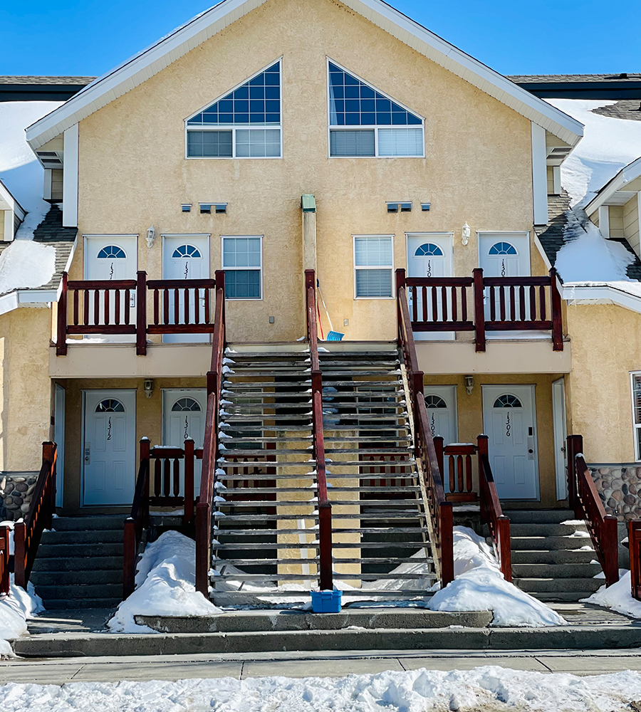 The entrance to a two storey townhouse unit at Stanford Fernie Resort featuring concrete stairs, large upper and lower floor windows and a layer of cobblestones providing an accent to a wall.