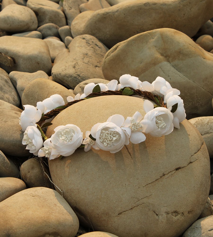 A bridal headband made entirely of white roses lay amongst smooth off-white cobblestones.