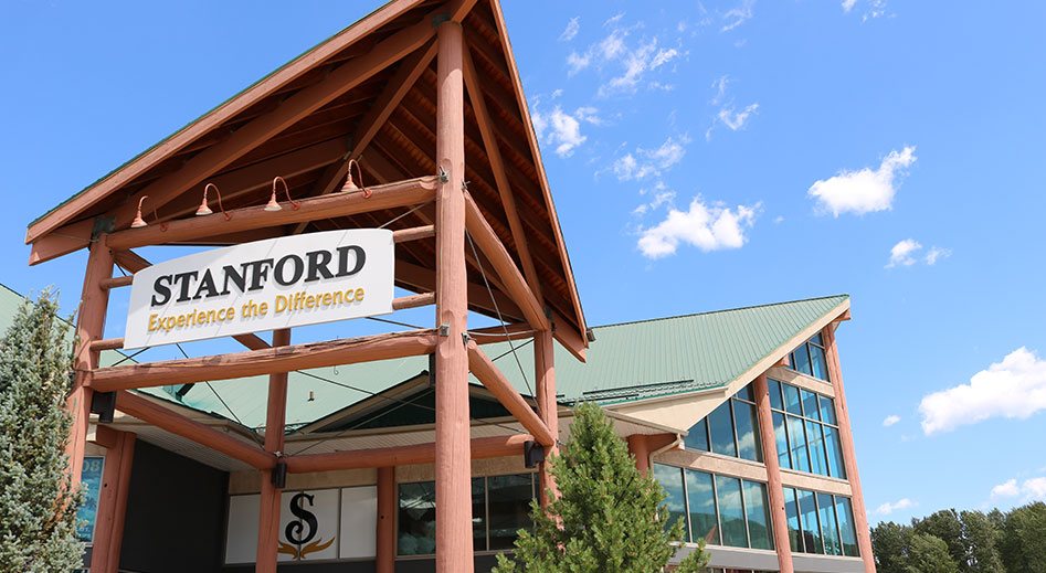 A skyward view of clear blue skies, the multiple triangular roof structures of the Stanford Fernie hotel and the portico bearing a sign of the corporate logo and slogan.
