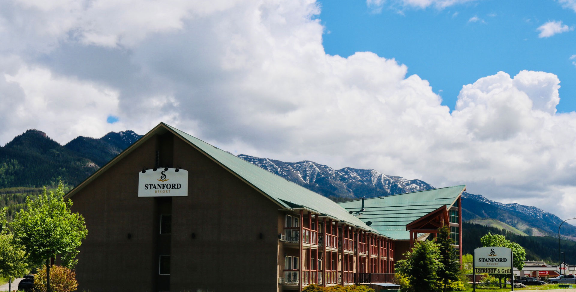 A skyward view of the multiple levels of picture windows of the Stanford Fernie Resort with its' corporate logo placed over the entrance and the log built portico bearing the large rectangular company sign.