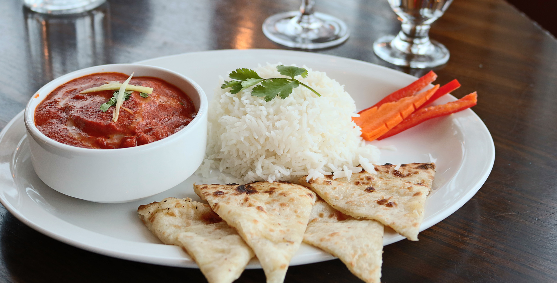 A round white plate serves a round container of red dipping sauce, dosas, white rice topped with parsley and carrots and red pepper garnishes at the Tandoor & Grill restaurant at Stanford Fernie Resort.